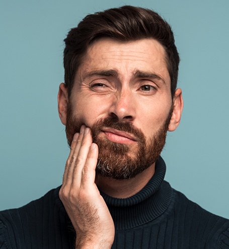 Bearded man rubbing his jaw in pain