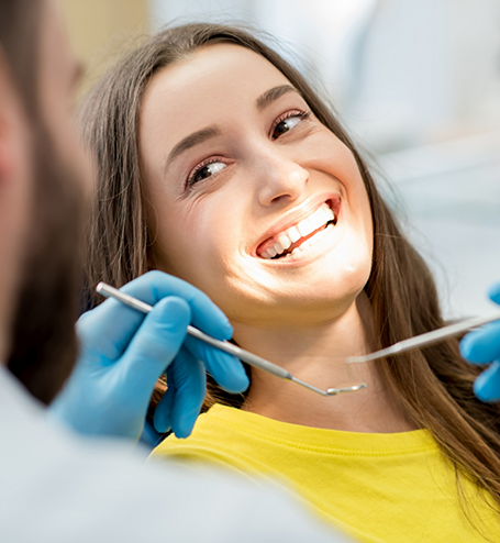 Female patient in yellow shirt smiling up at dentist